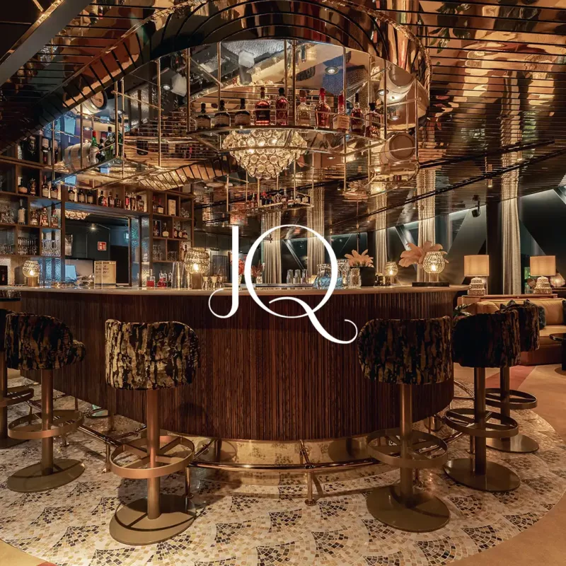 The JQ Bar, a curved wooden bar beneath a mirrored ceiling and chandelier